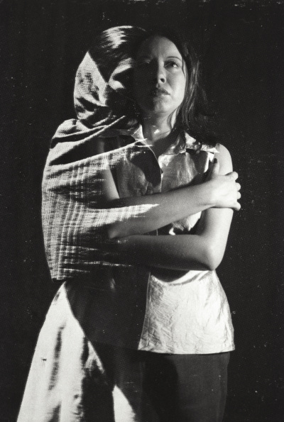 Black and white double exposure photo of a woman facing the camera, arms crossed. To the left, half a woman is visible, covered by a draping scarf, where her left arm should be connects/melds into the other woman's arm, so they are sort of hugging each other/themselves.